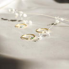The Venice Initial Birthstone Ring, a delicate gold ring adorned with a personalized initial and colorful birthstones, is displayed on light fabric next to white dried flowers.