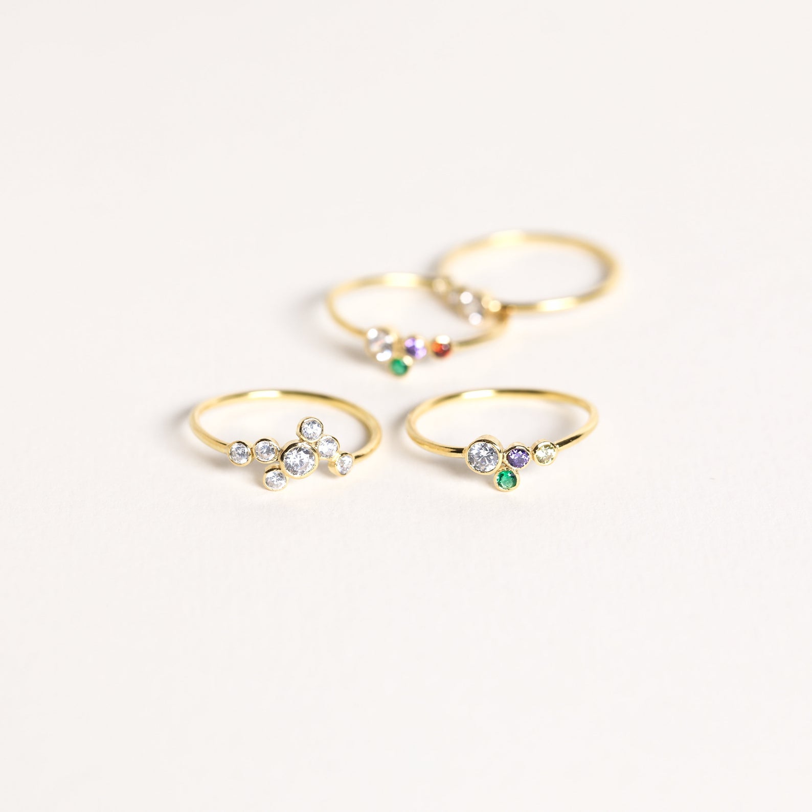 The Cluster Birthstone Ring, a delicate gold piece adorned with colorful gemstones and diamonds, is displayed on a light background.