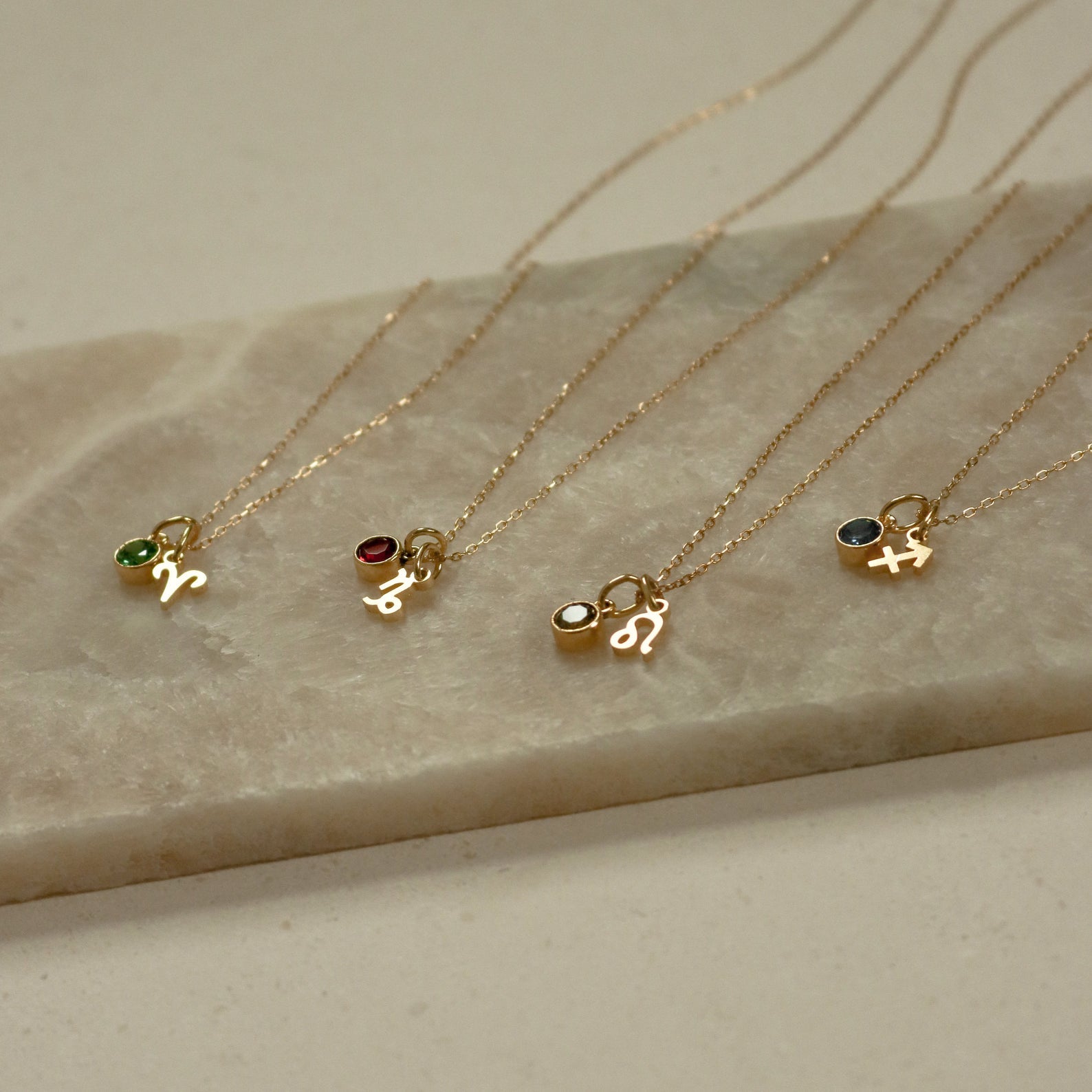 Four Zodiac Birthstone Necklaces with colorful gemstones on marble—perfect personalized jewelry or birthstone gift for any star sign.