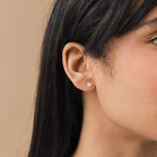 Close-up of a woman's ear with straight dark hair, wearing Pave Round Studs—small, round gold earrings ideal for those who prefer subtle glam jewelry over larger or sparkling pave styles.