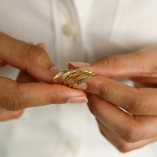 Close-up of hands holding several Ann Skinny Name Rings in Rose Gold, each engraved with a name—ideal as stackable rings or a thoughtful Christmas gift for her, shown against a white shirt background.
