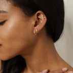 Close-up of a woman’s ear wearing two gold Willow Huggies and a small stud on the upper ear, highlighting her smooth skin.