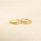 Two Gina Pave Signet Rings, featuring gold bands accented with small sparkling stones, are placed side by side on a light, textured surface.