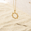 Gold sun-shaped pendant necklace resting on sand, featuring a hollow center and spiked edges embellished with pave set stones.