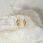Willow Huggies: Gold hoop earrings with square, clear stones set in 925 sterling silver, shown on a textured white stone surface.