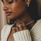 A woman in a cream knit sweater, wearing freshwater pearl earrings, necklace, and the Pearl Beaded Ring, creates a classy accessory ensemble as she gazes downward.