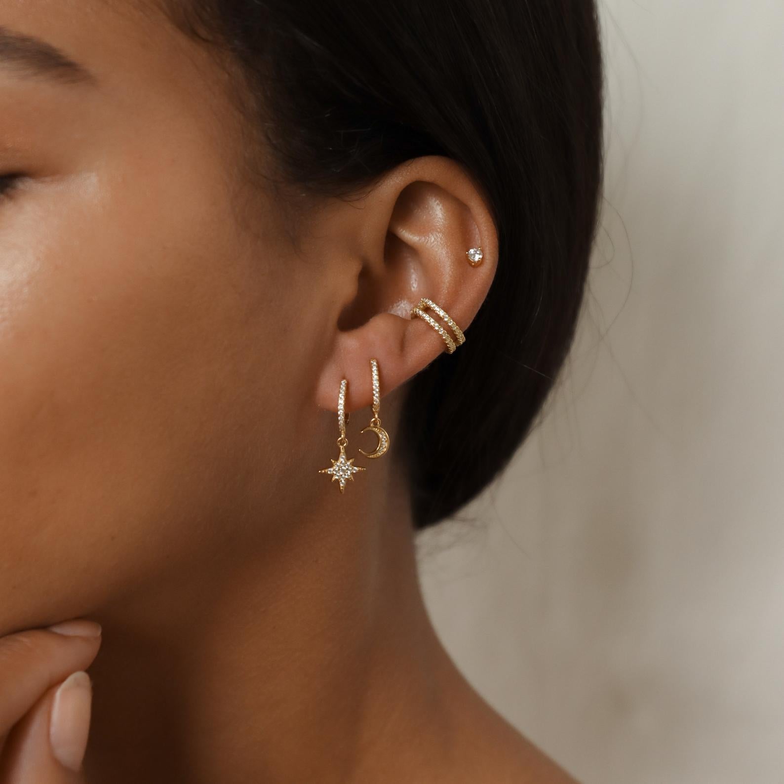 Close-up of a woman’s ear adorned with Moon and Star Huggies in Sterling Silver, her hand gently resting near her chin.