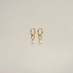 The Hazel Pearl Hoops are gold hoop earrings with dangling white pearls, a modern jewelry standout, elegantly showcased against a plain light background.