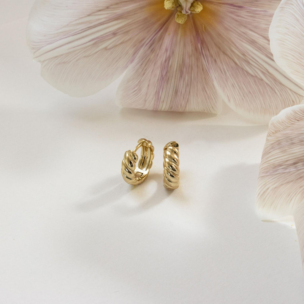 Morgan Croissant Hoops showcased on a white surface with pale pink flowers in the background—a chic accessory that channels French girl style with modern flair.