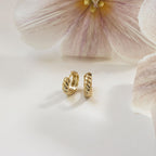 Morgan Croissant Hoops showcased on a white surface with pale pink flowers in the background—a chic accessory that channels French girl style with modern flair.