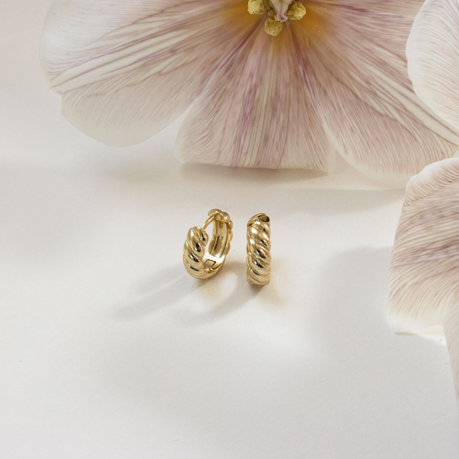 Morgan Croissant Hoops showcased on a white surface with pale pink flowers in the background—a chic accessory that channels French girl style with modern flair.