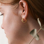 Close-up of a woman's ear wearing the Morgan Croissant Hoops, capturing the French girl aesthetic with part of her face and hair visible—modern gold earrings designed for effortless style.