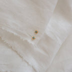 Two Mara Studs, featuring gold and a hint of turquoise, are displayed elegantly on a white cloth.