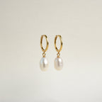 The Maggie Pearl Drop Hoops are gold modern earrings with dangling oval white pearls, displayed against a plain light background—ideal for minimal jewelry lovers.