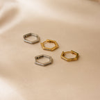 Two pairs of Parker Pave Hexagon Huggies—one silver, one gold—featuring small crystals for sparkle, displayed on beige fabric. A chic ear accessory.