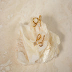 The Moon and Star Huggies in Sterling Silver, featuring celestial-inspired designs with crystal accents, are displayed on a white translucent rock against a beige background.