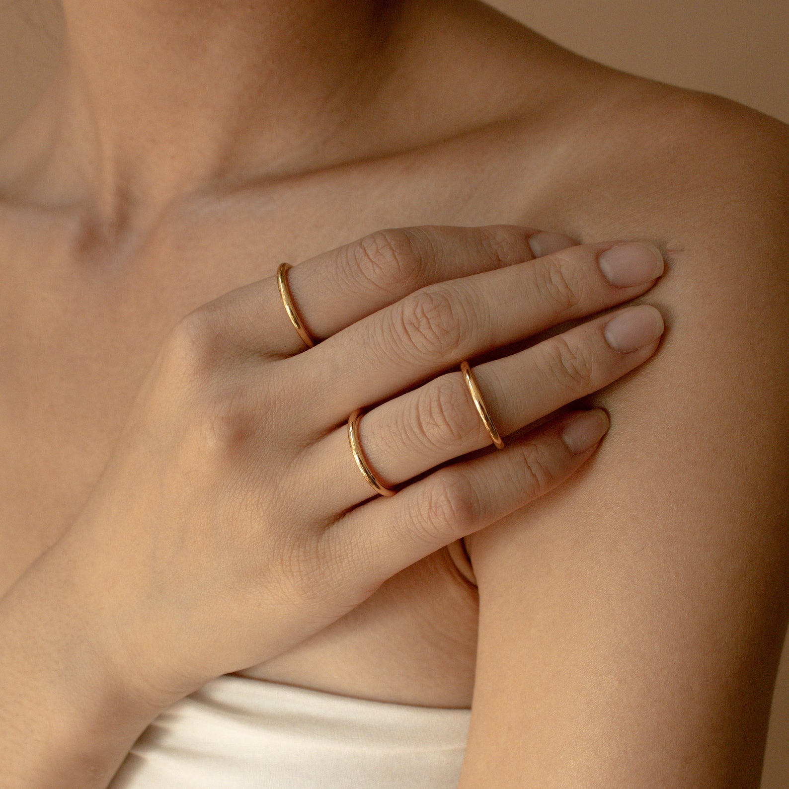 A person wearing three Minimal Stacking Rings rests their hand on their bare shoulder against a neutral background.