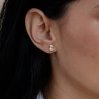 Close-up of a woman's ear wearing Emerald Diamond Studs, highlighting the elegance of rectangular, clear gemstones in a gold prong setting and showcasing the timeless appeal of classic stud earrings.