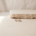 Emerald Diamond Studs featuring gold prong-set rectangular clear stones, displayed on a light textured surface—a timeless update to classic stud earrings.