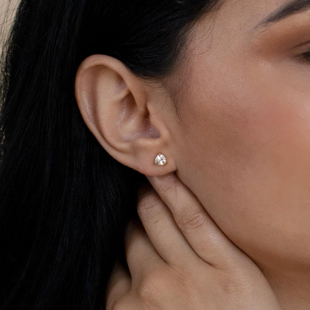 A close-up of a woman's ear wearing classic jewelry—Triangle Diamond Studs—while her hand rests near her neck.