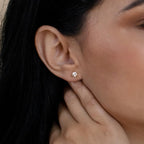 A close-up of a woman's ear wearing classic jewelry—Triangle Diamond Studs—while her hand rests near her neck.