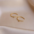 The Rylee Diamond Wire Earrings, featuring two gold open hoops set with small diamonds, rest on soft beige satin fabric, adding a modern touch of sparkle.