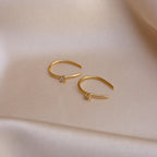 The Rylee Diamond Wire Earrings, featuring two gold open hoops set with small diamonds, rest on soft beige satin fabric, adding a modern touch of sparkle.