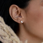 Close-up of a woman's ear wearing Round Diamond Studs, with classic elegance reflected in the solitaire diamonds, as beige pampas grass softens the foreground.