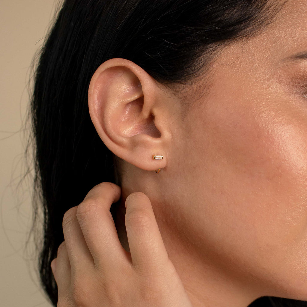 A close-up of a woman's ear wearing Shayla Baguette Huggies, highlighting the elegant baguette-shaped diamond hoop earrings.