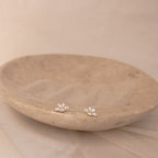 Marquise diamond stud earrings set in 18K gold, arranged in a delicate floral cluster on a textured beige dish.