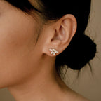 Marquise diamond stud earrings in 18K gold with small pavé diamonds, worn on the earlobe against warm skin tone 