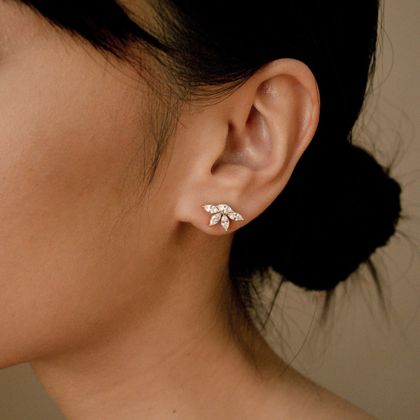 Marquise diamond stud earrings in 18K gold with small pavé diamonds, worn on the earlobe against warm skin tone 