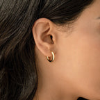 Close-up of a woman’s ear wearing Madison Hoops, small gold minimalist earrings, with her dark hair partially visible.