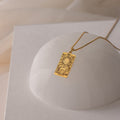 The Tarot Necklace in Box Chain features a gold rectangular pendant with a sun and celestial design inspired by the Major Arcana, shown on a white dome.
