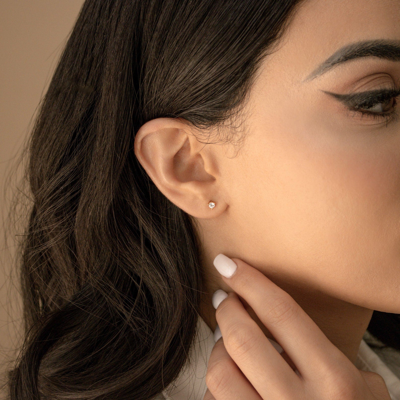Woman with dark hair wears Elena Diamond Studs, touching her ear with manicured fingers for an elegant, everyday style.