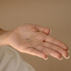 A hand holds three Elena Diamond Studs, each featuring a unique colored stone, against a beige background—perfect everyday earrings to complement any outfit.