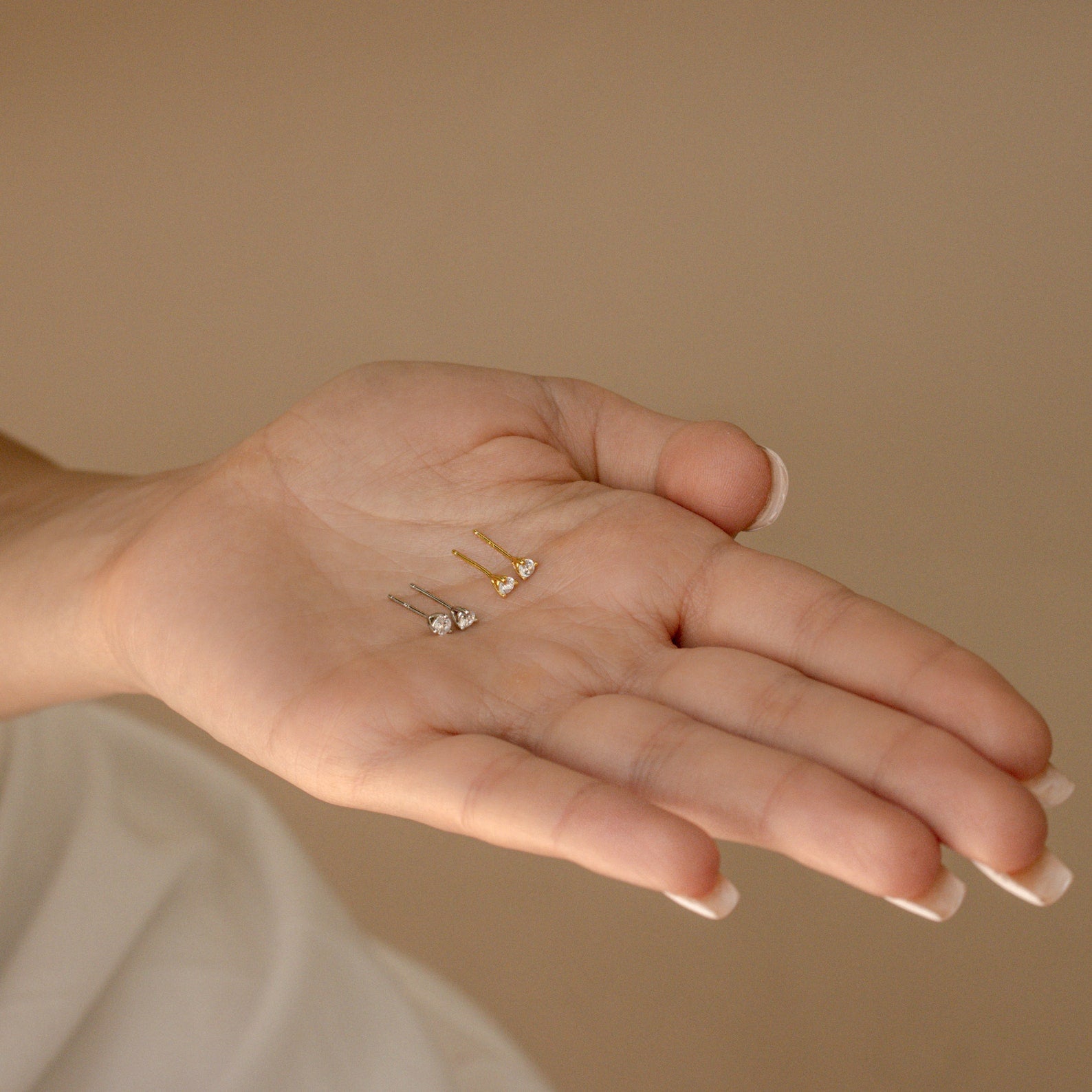 A hand holds three Elena Diamond Studs, each featuring a unique colored stone, against a beige background—perfect everyday earrings to complement any outfit.