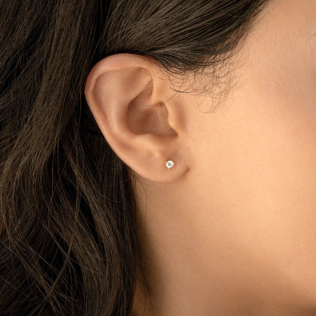 Close-up of a woman's ear wearing Elena Diamond Studs—small, round diamond earrings that are perfect minimal studs for everyday wear—her dark hair partially visible.