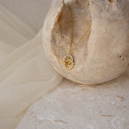 Sun & Moon Eternity Necklace featuring a gold sun and moon design, displayed on a textured beige stone surface.