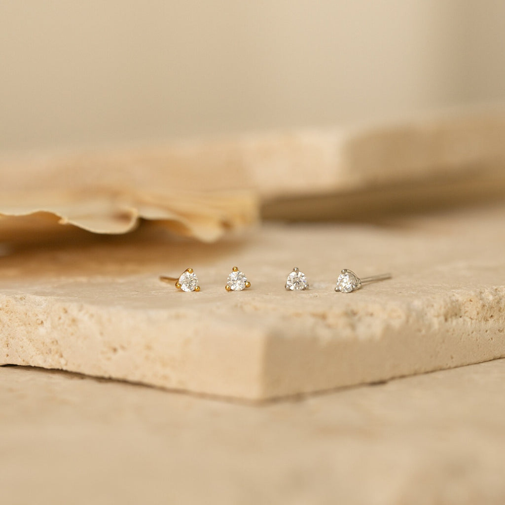 Two pairs of Elena Diamond Studs, each featuring three stones, are displayed on light stone surfaces—perfect as everyday earrings.