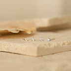 Two pairs of Elena Diamond Studs, each featuring three stones, are displayed on light stone surfaces—perfect as everyday earrings.