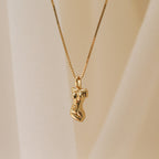 The Kinn Body Necklace features a gold pendant shaped like a stylized human torso, inspired by the Venus de Milo, displayed against a soft beige background—a refined and empowering jewelry piece.