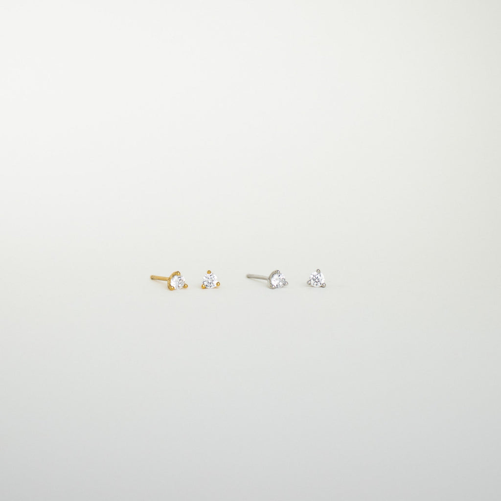 The Elena Diamond Studs set includes two pairs of minimal diamond stud earrings—one gold, one silver—each with a clear gemstone, perfect for elevating your everyday earring collection.