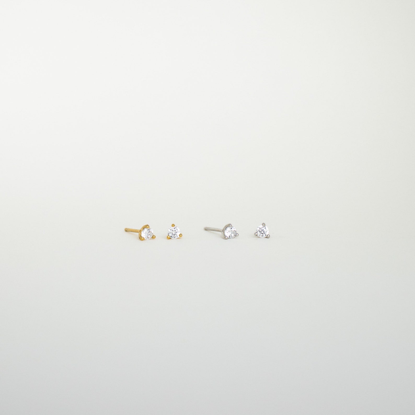 The Elena Diamond Studs set includes two pairs of minimal diamond stud earrings—one gold, one silver—each with a clear gemstone, perfect for elevating your everyday earring collection.