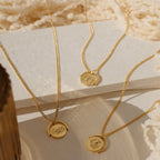 Three Zodiac Spinner Necklaces with round engraved astrological pendants are displayed on textured cream surfaces in sunlight.