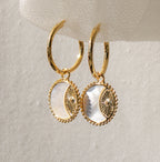 Pia Pearl Coin Hoops feature gold hoops with round white mother-of-pearl pendants and decorative gold details, adding a touch of boho elegance to any outfit.