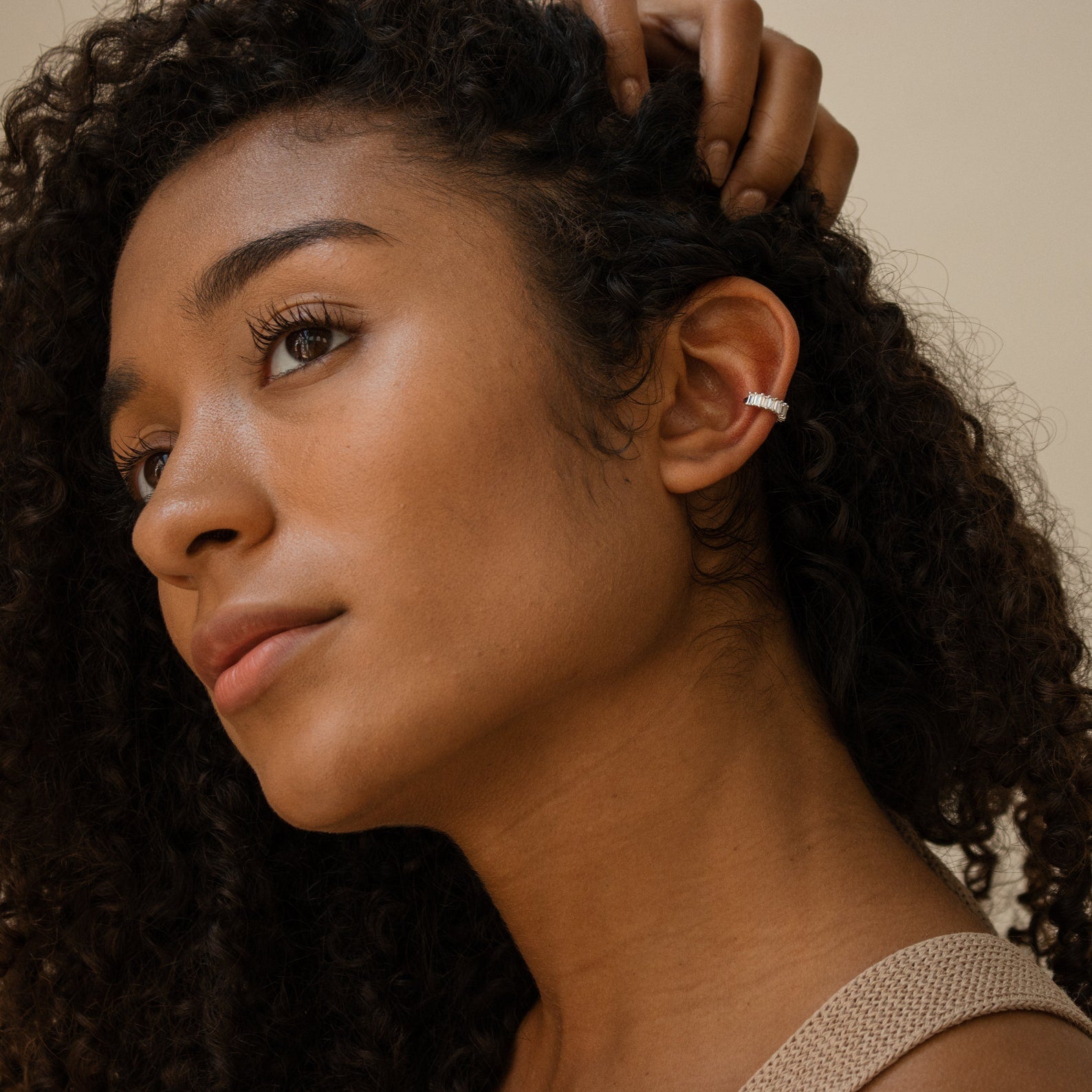 A woman with curly hair wears Baguette Ear Cuffs in silver, gazing thoughtfully to the side with her hand in her hair.