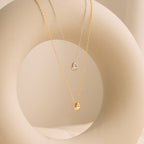 Two Nugget Necklaces—one gold, one silver—each with a delicate pendant, hang elegantly on a smooth circular display, making them the perfect pair for lovers of dainty necklaces.
