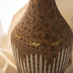 The Preppy Multiple Name Necklace in Box Chain, featuring Naomi, Evelyn, and Jessica in a youth-inspired font, is draped over a textured brown vase.