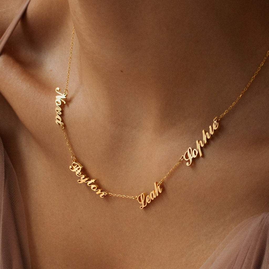 The Carrie Multiple Name Necklace in Rose Gold features a delicate chain and multiple names—Noah, Peyton, Leah, and Sophie—elegantly scripted in cursive on a woman’s neck.